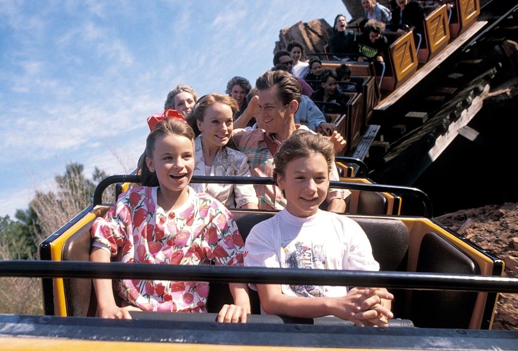 Group of excited people of various ages on a roller coaster with hands raised; clear skies
