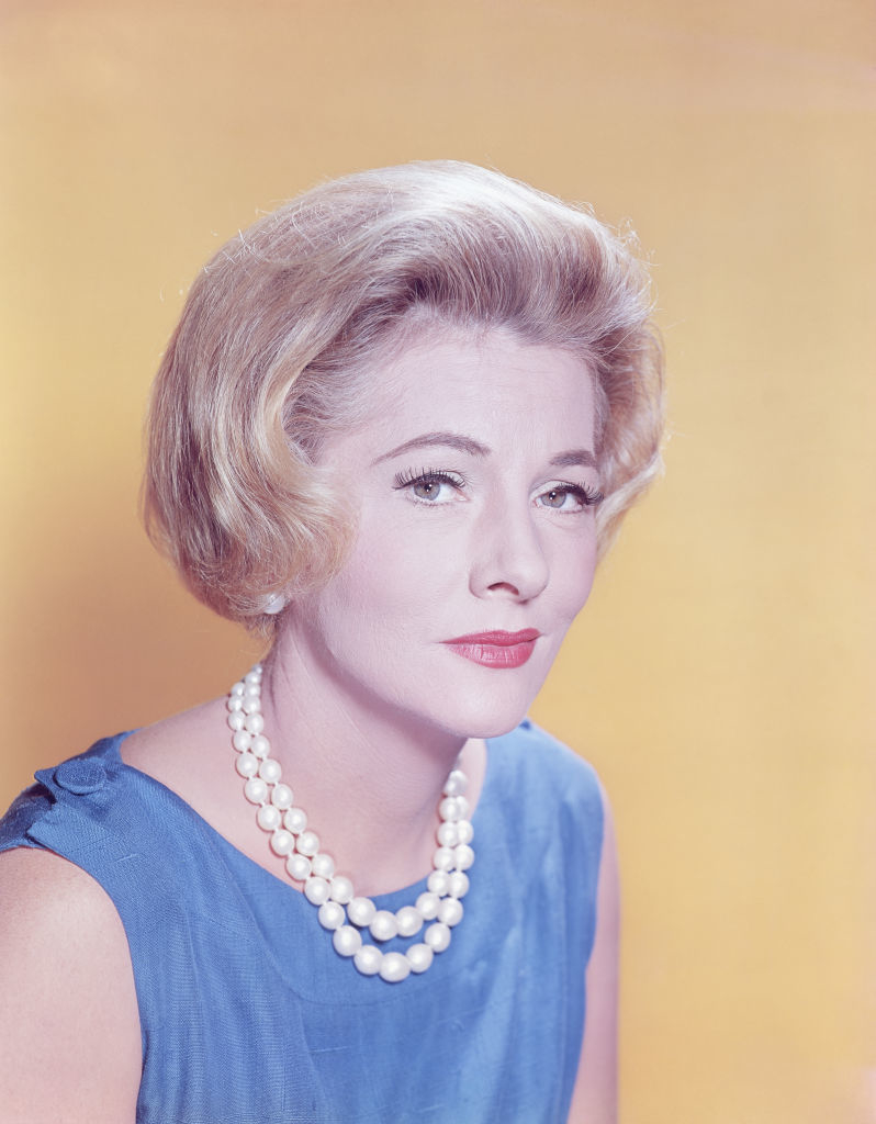 Joan in a sleeveless dress and pearl necklace, facing the camera with a slight tilt to her head
