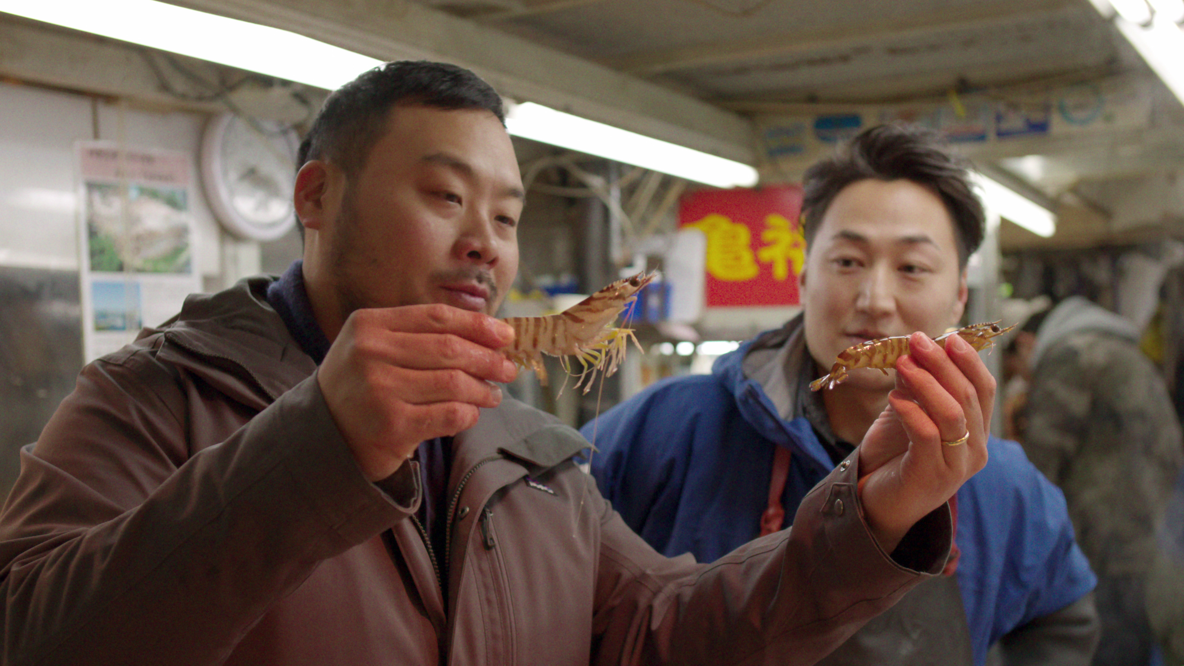 Two men smiling, holding and examining live shrimp at a seafood market