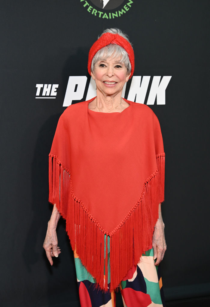 Rita Moreno at an event, wearing a poncho with fringe details and a matching beret