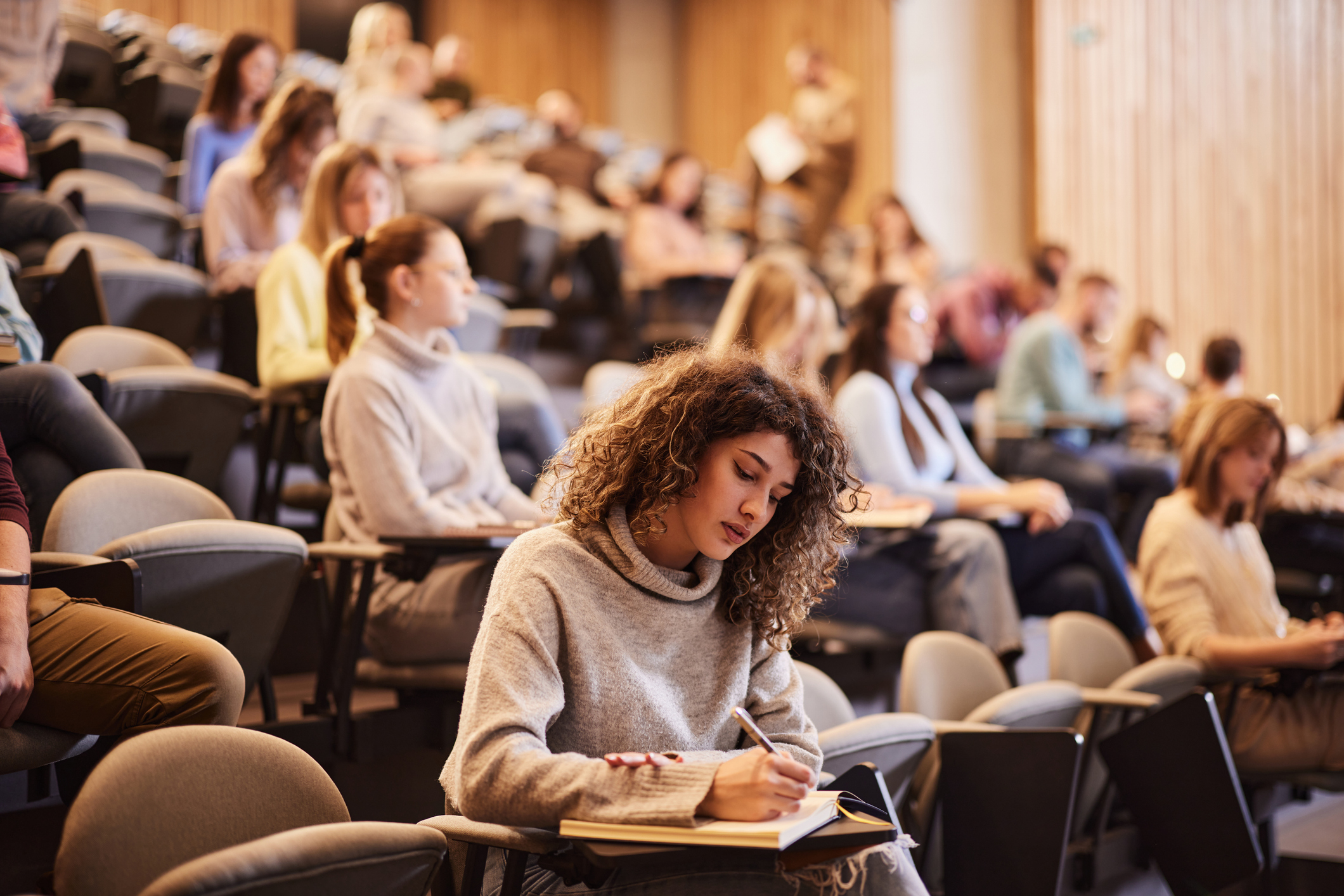 A student takes notes in a lecture hall filled with attendees