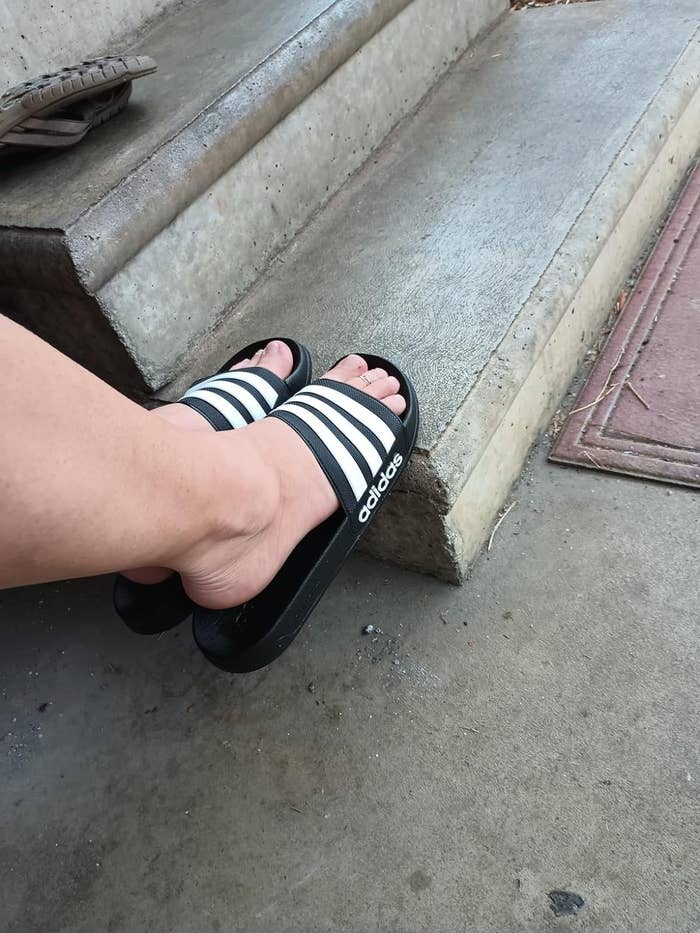 Foot wearing Adidas slide sandal on concrete steps, for an article on casual footwear shopping
