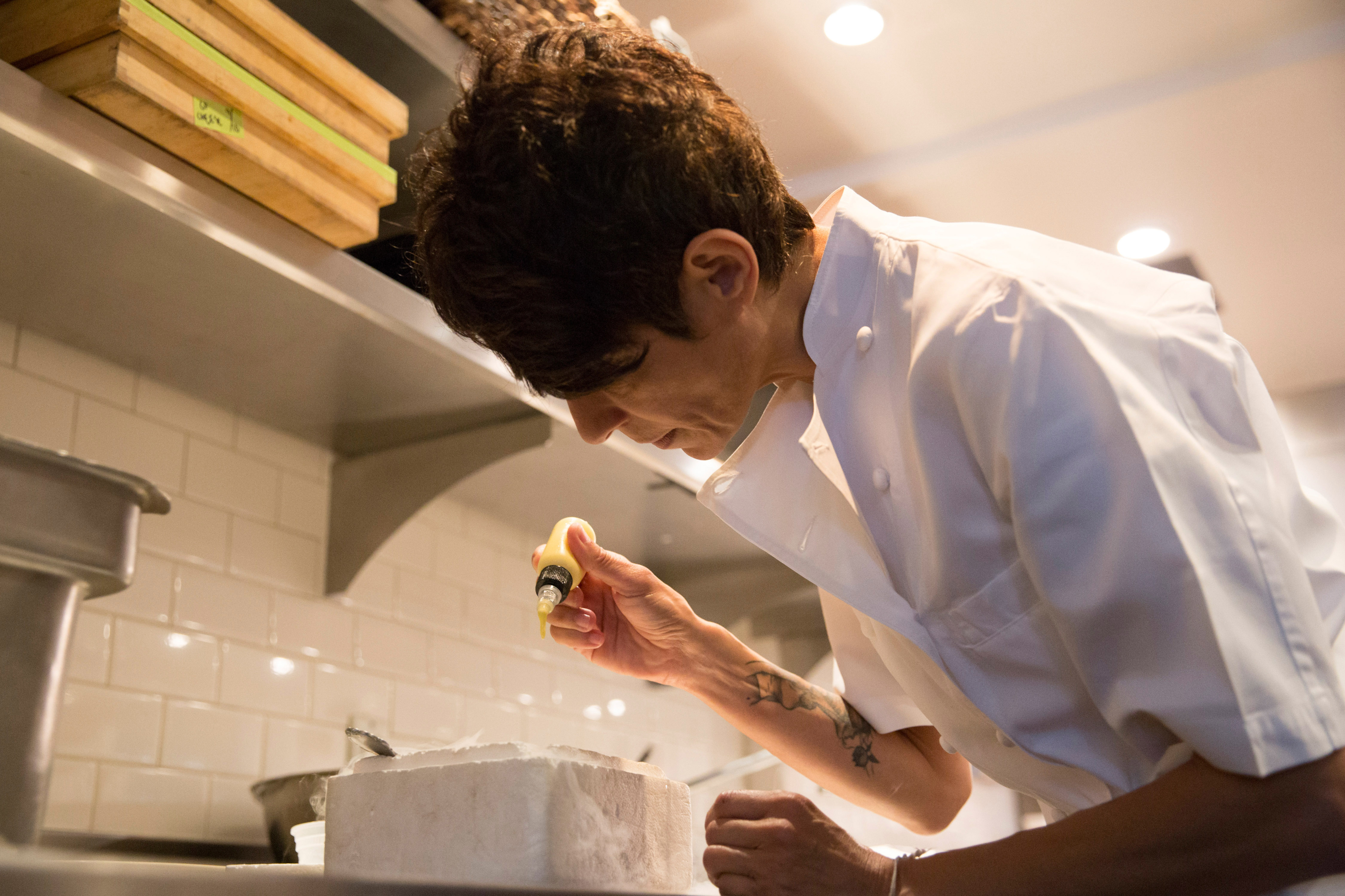 Chef in white uniform meticulously garnishing a dish in a professional kitchen