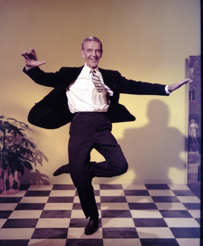 Fred Astaire in a classic dance pose wearing a suit and striped tie with a shadow on the wall