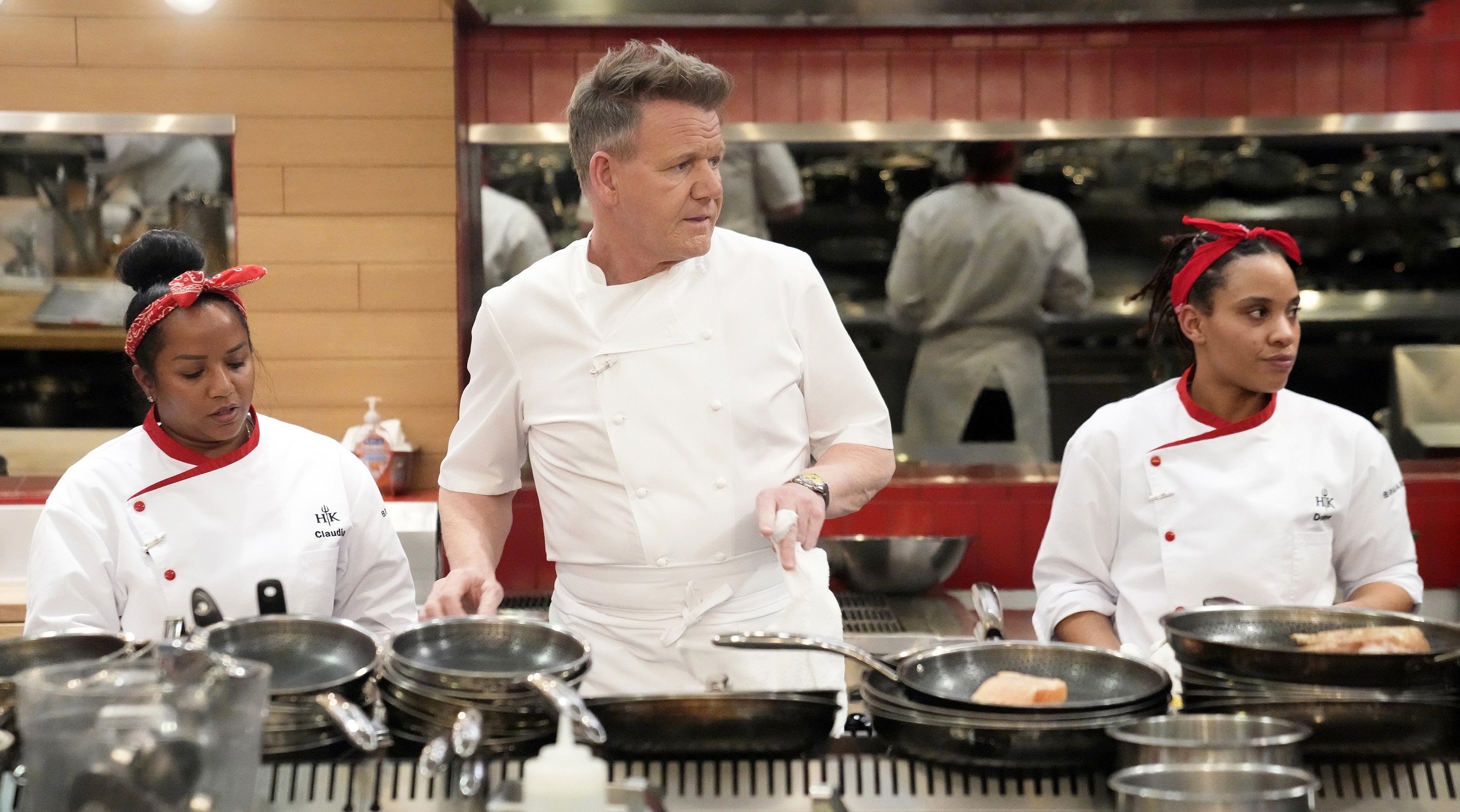 Gordon Ramsay with two chefs in a kitchen, overseeing cooking activities