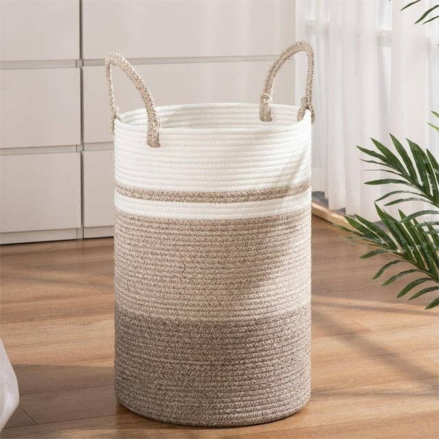 Woven laundry basket in a two-tone design next to a plant