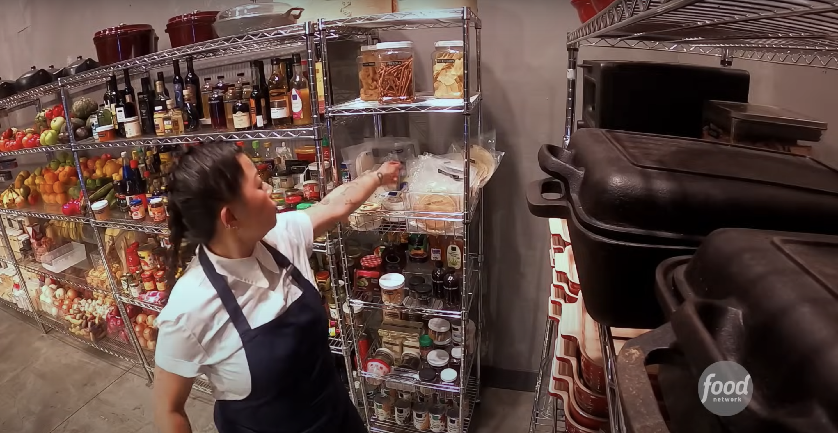 Chef in an apron reaches for ingredients on a pantry shelf in a professional kitchen