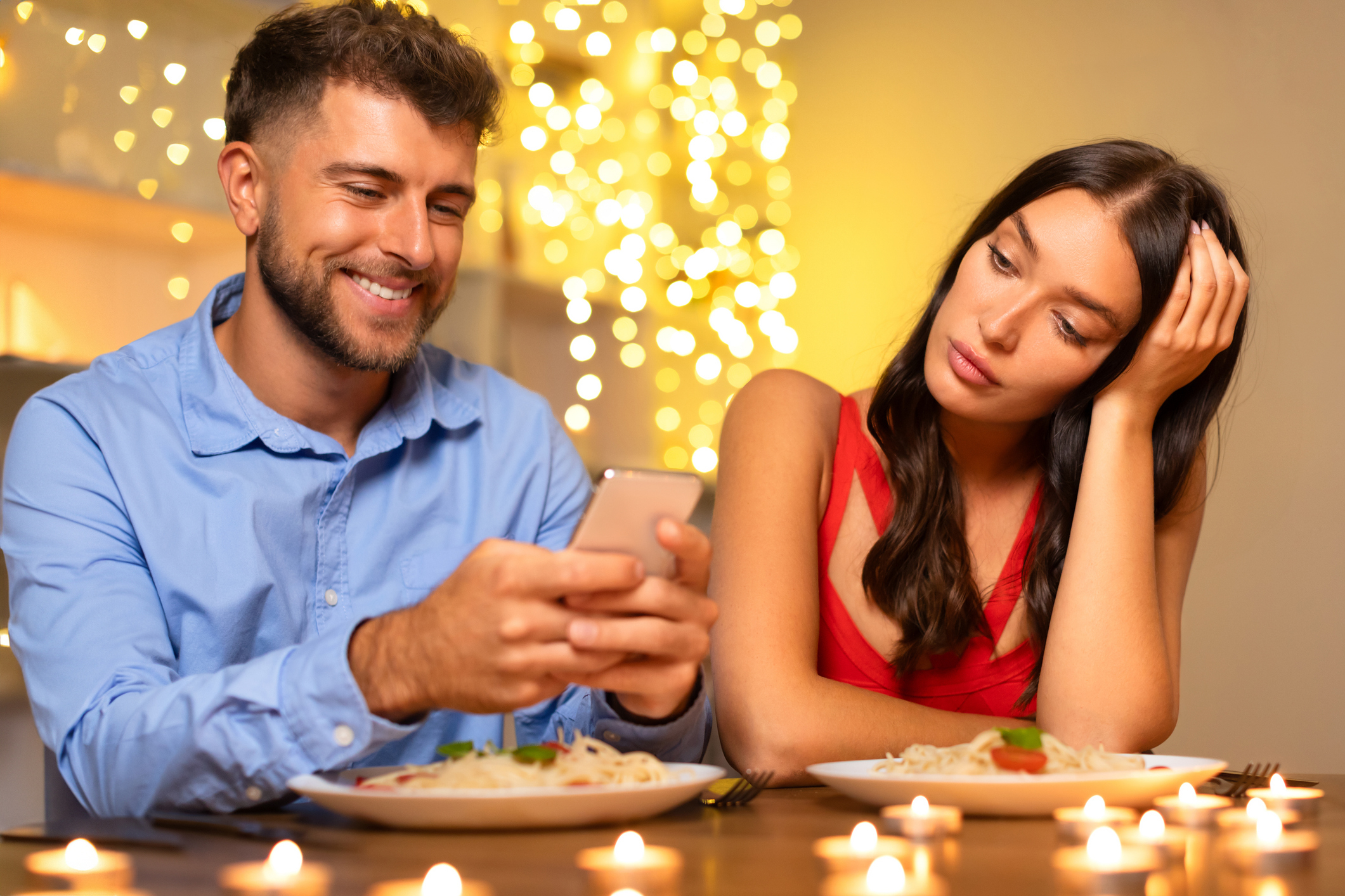 Man smiling at phone on date while woman looks bored