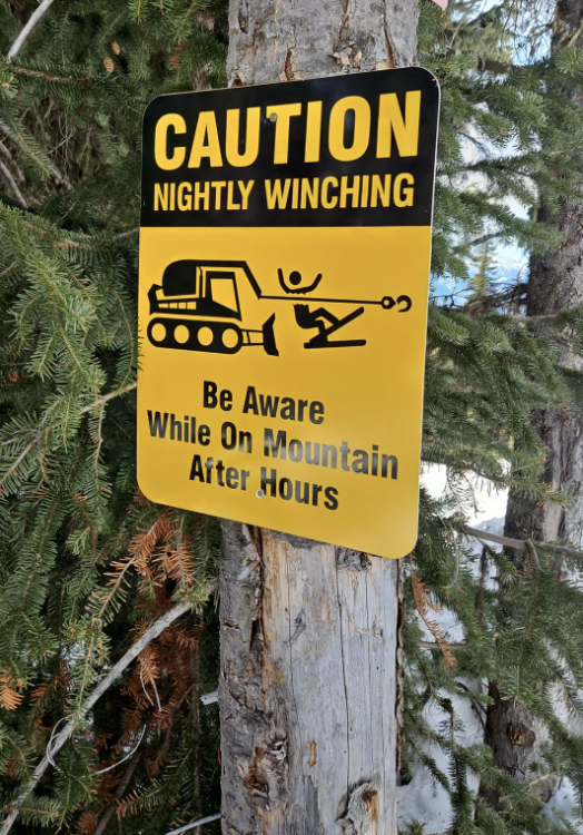 Caution sign warning of nightly winching on a mountain with graphic illustrating the hazard