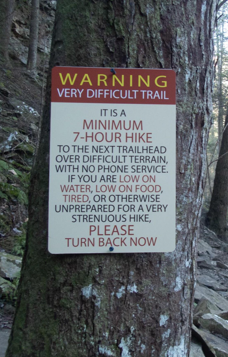 Warning sign on a tree about a very difficult hiking trail with no phone service, advising unprepared hikers to turn back