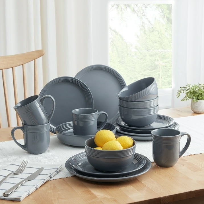 A set of dark-toned dinnerware including plates, bowls, and mugs arranged on a dining table