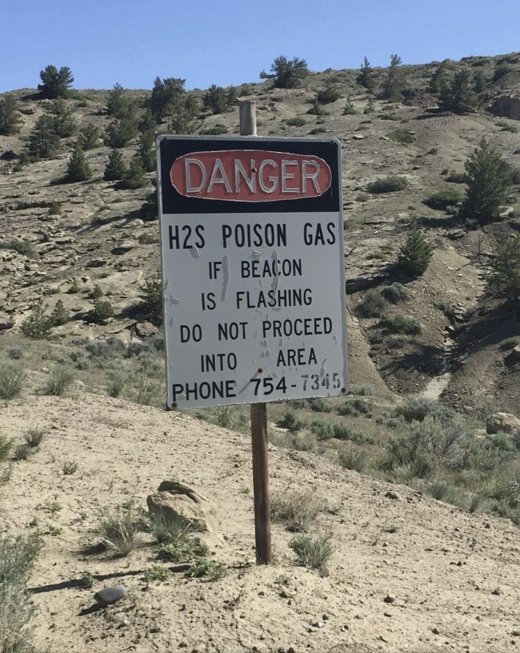 Warning sign about H2S poison gas, instructing not to enter area if beacon flashes, with a contact phone number