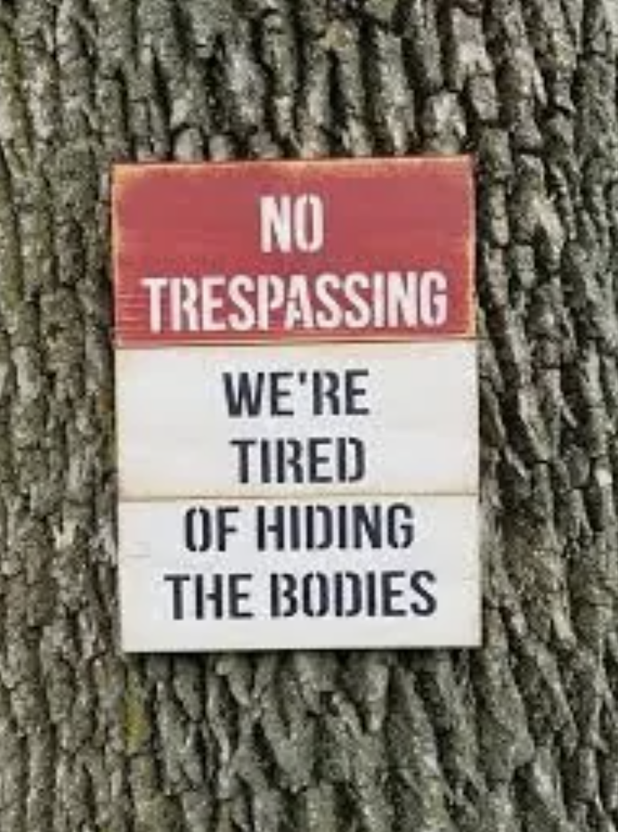 Sign on tree reads &quot;NO TRESPASSING - WE&#x27;RE TIRED OF HIDING THE BODIES&quot; as a humorous warning