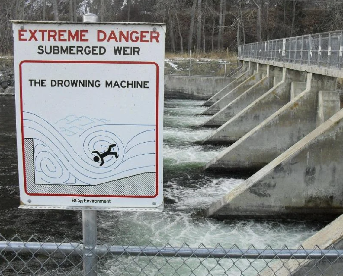 Warning sign by river illustrating the danger of a submerged weir known as &quot;The Drowning Machine.&quot;