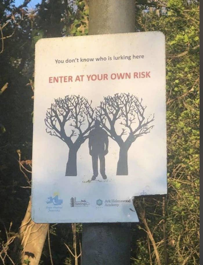 Warning sign with a silhouette between trees, text reads &quot;Enter at your own risk,&quot; indicating a potentially unsafe area