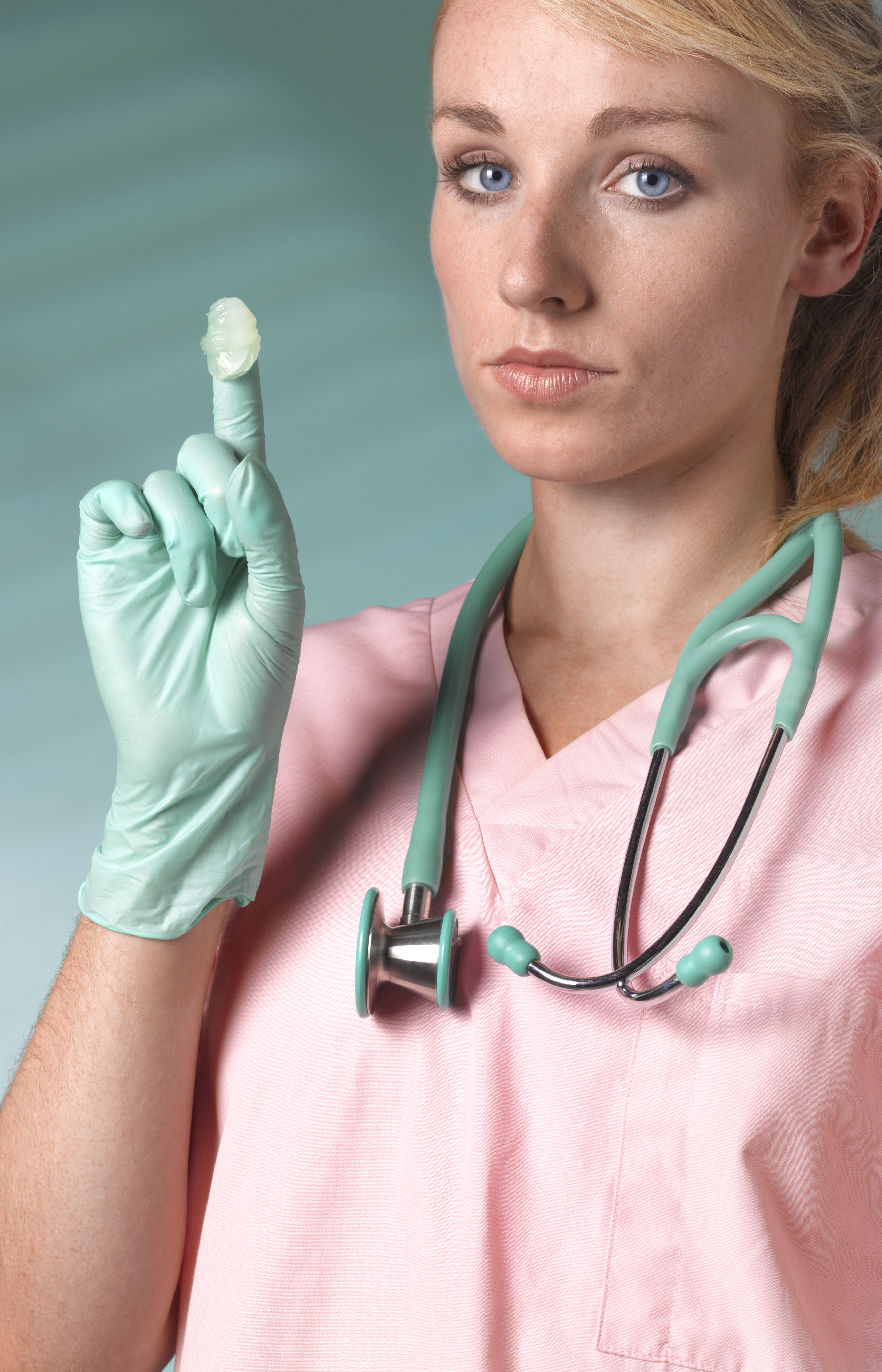 Medical professional in scrubs with a stethoscope holding up a dab of lubricant on her gloved finger