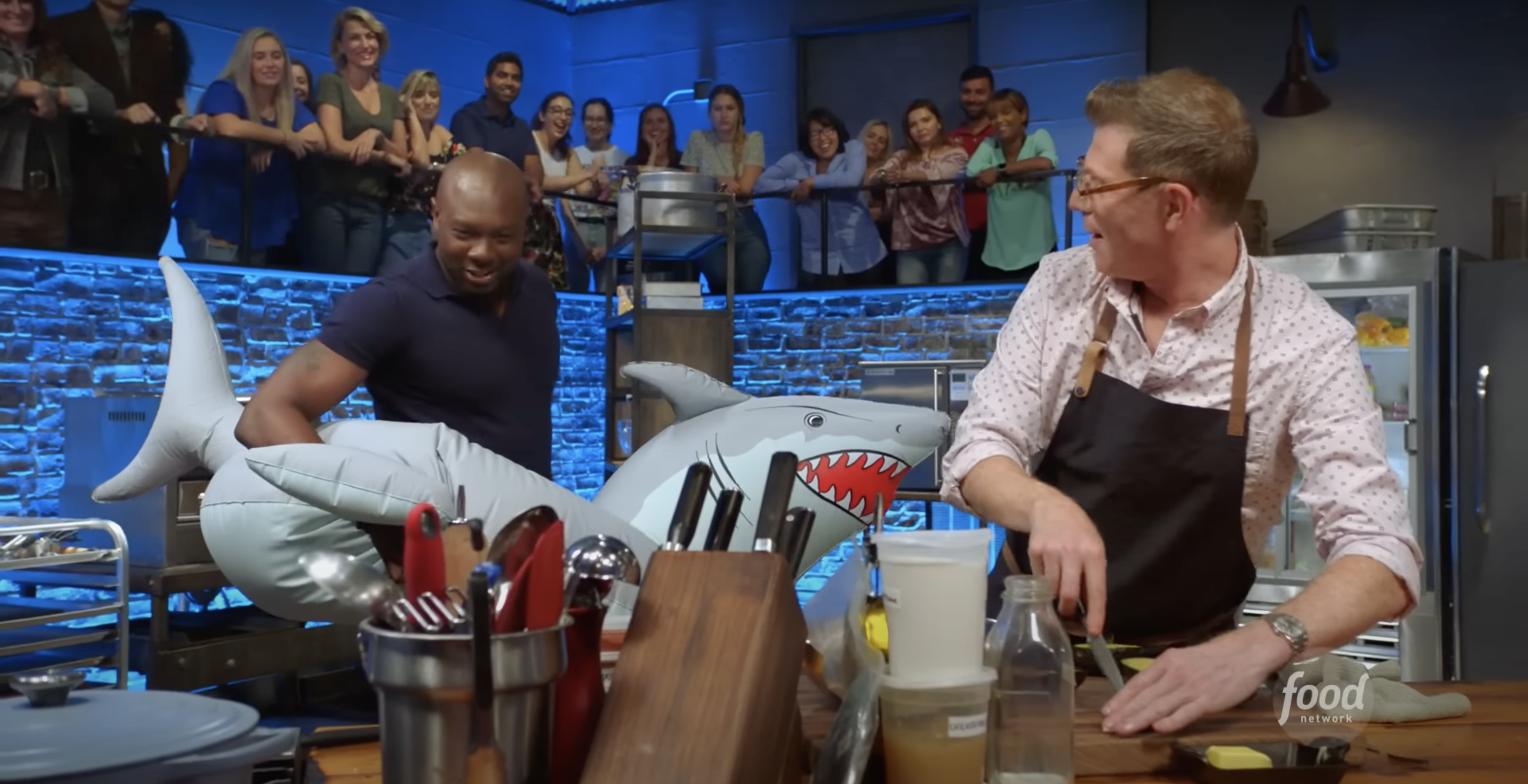 Two chefs in an animated kitchen competition with a shark-themed setup