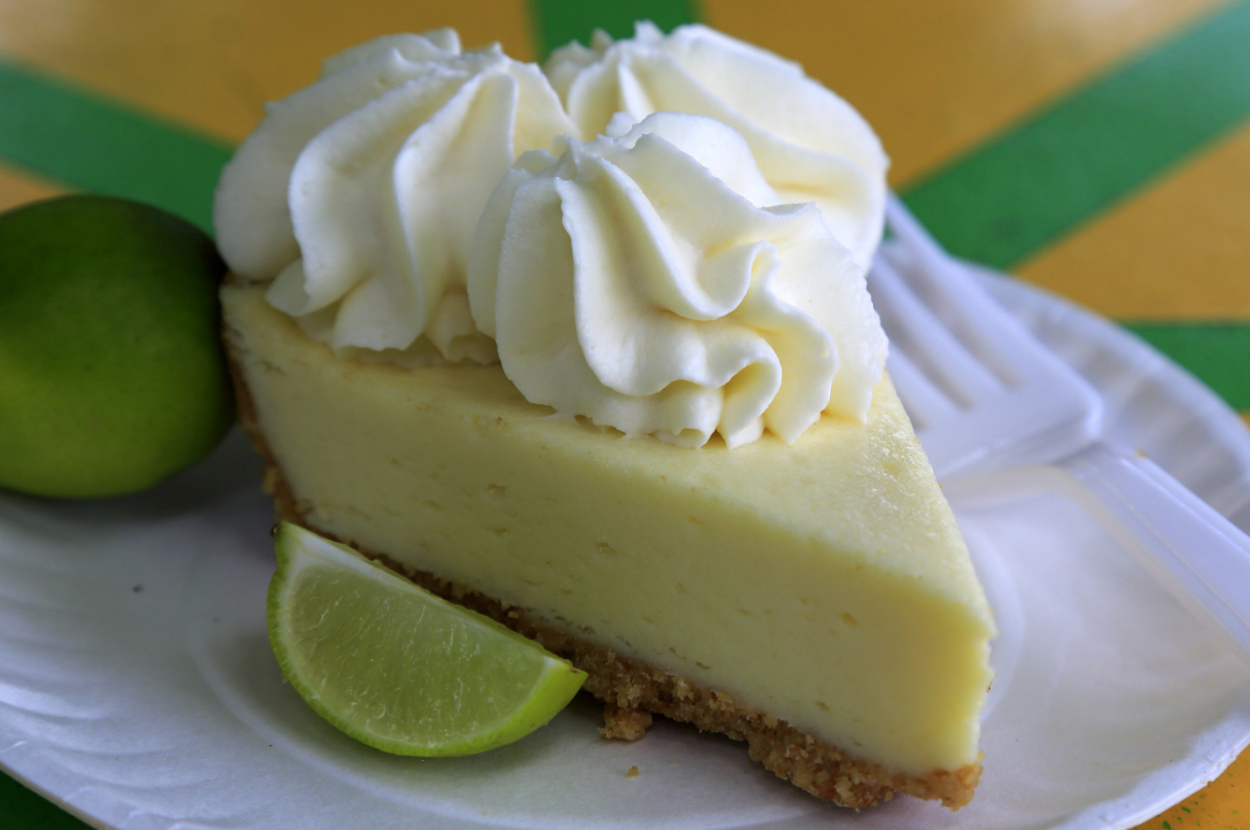 Slice of key lime pie with whipped cream on a plate, accompanied by a lime wedge