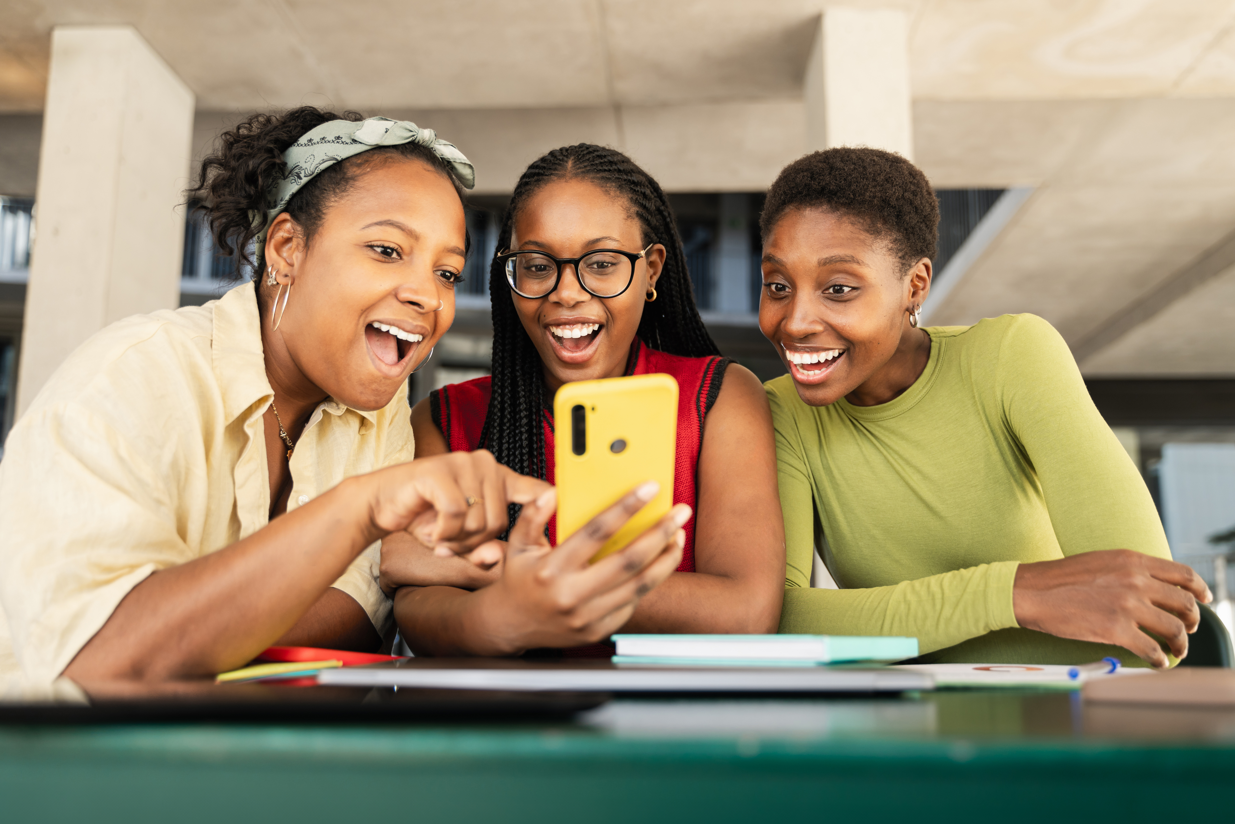 Three women smiling at a smartphone together, possibly reviewing work content or financial data
