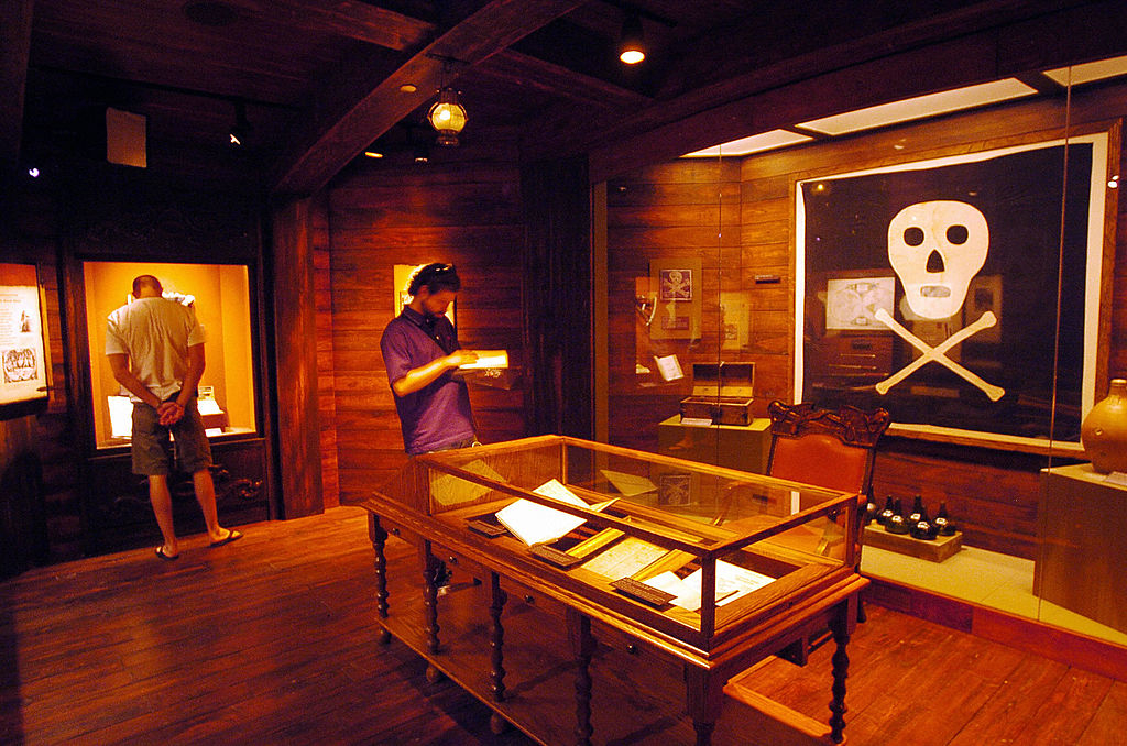 Two individuals observing exhibitions inside a museum with artifacts displayed in glass cases and on walls