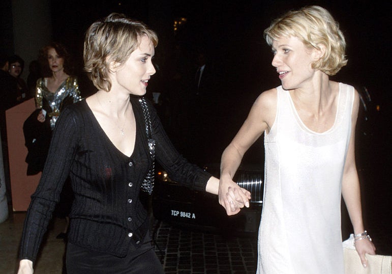 Winona Ryder in a black dress holding hands with Gwyneth Paltrow wearing a white dress