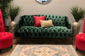 Velvet green sofa with tufted design and decorative pillows flanked by two red ottomans and metallic floor vases
