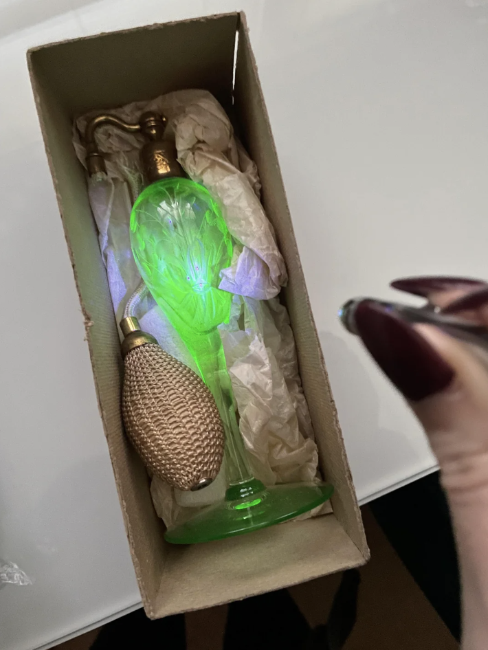 Hand holding a perfume bottle with intricate design, illuminated by light, presented in a box