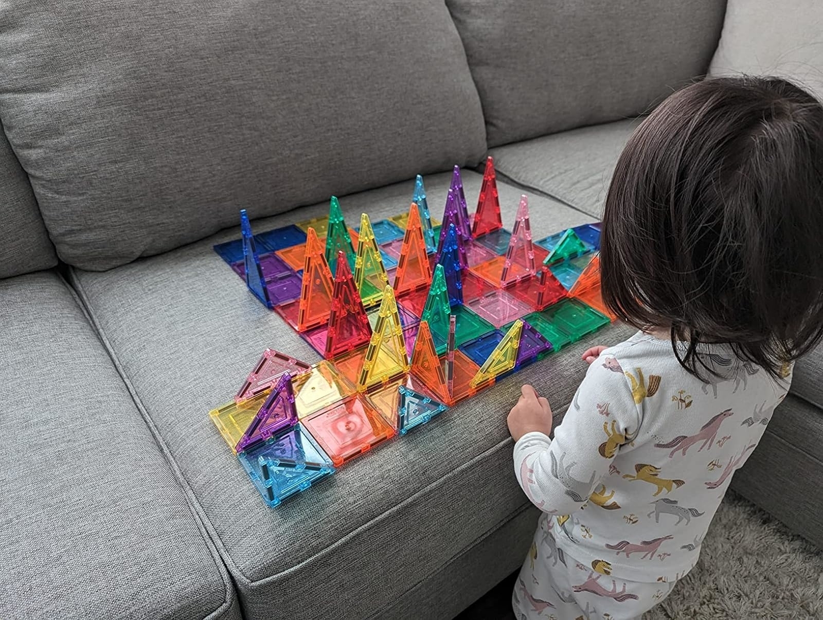 Child playing with colorful magnetic building blocks forming structures on a sofa