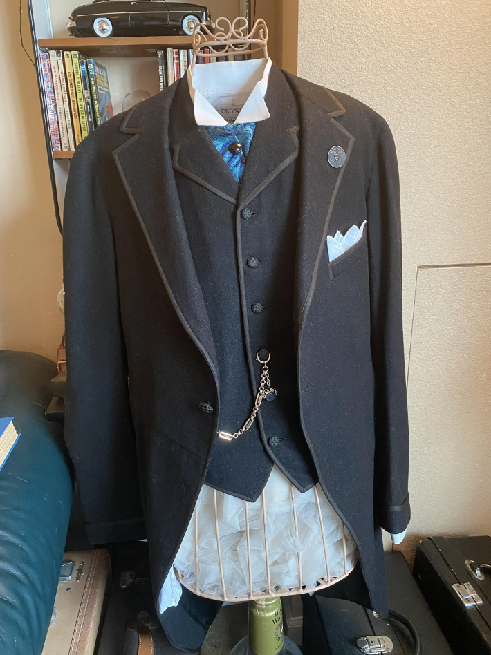 Vintage-style suit displayed with pinstripe trousers, chain accessory, and patterned tie