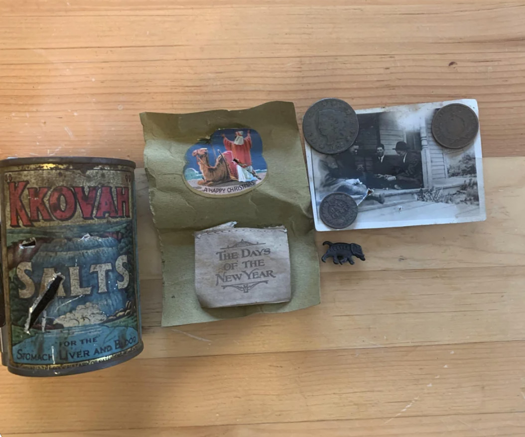 Assorted vintage items on a table, including an old tin, a photograph, coins, and paper cutouts with festive messages