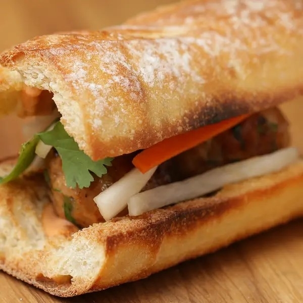 A close-up of a banh mi sandwich with crusty bread, herbs, and fillings