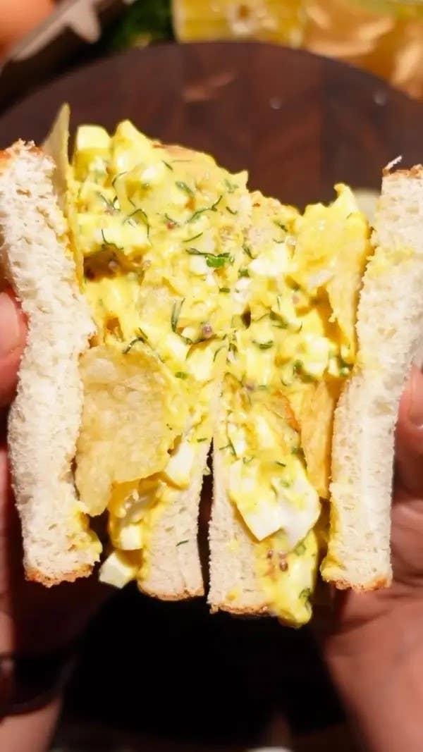 Egg salad sandwich with visible herbs, held open to show filling