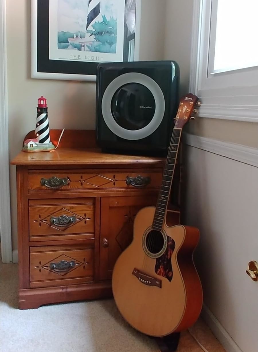A wooden dresser with a framed lighthouse art piece above, a washing machine, a striped figurine, and an acoustic guitar beside