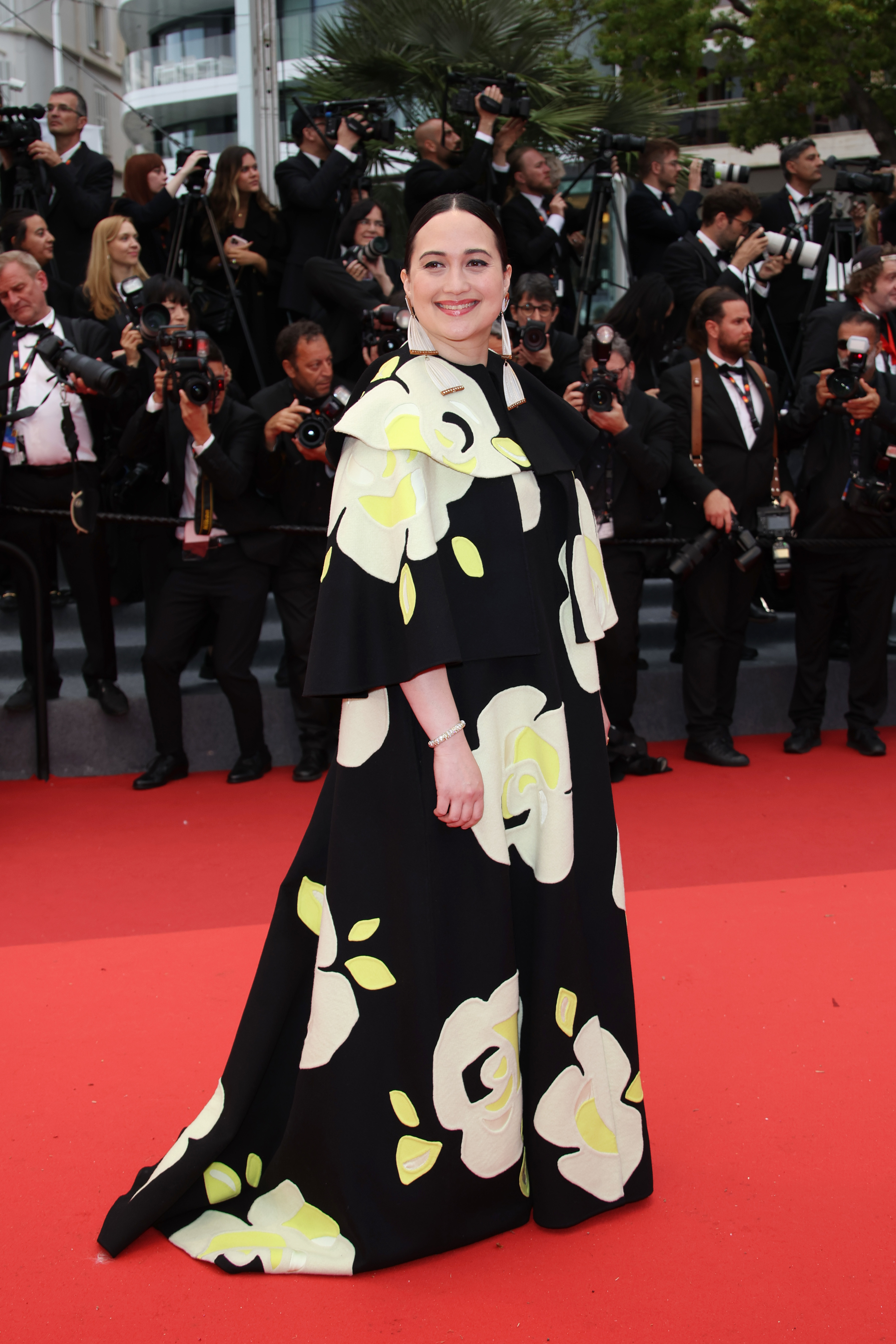 Woman in a floral patterned gown poses on the red carpet with photographers in the background