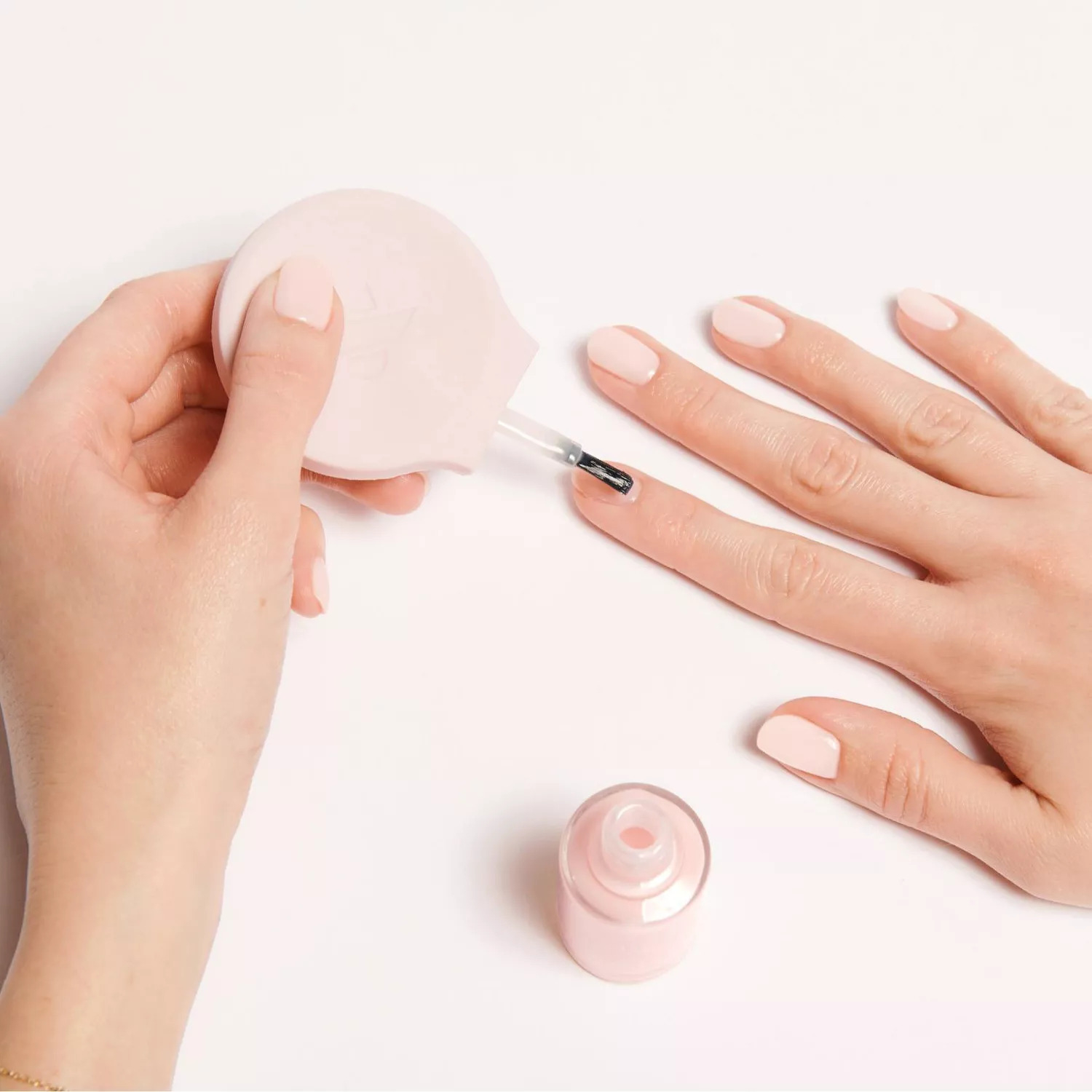 Hands applying nail polish with the round, flat handle attached to the brush