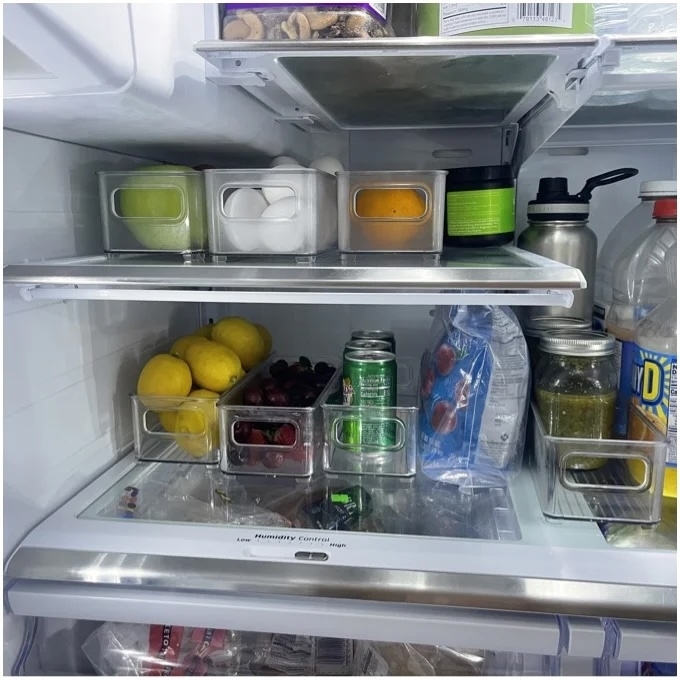 An organized refrigerator with clear storage bins and stacked beverages, showcasing efficient space usage for food items