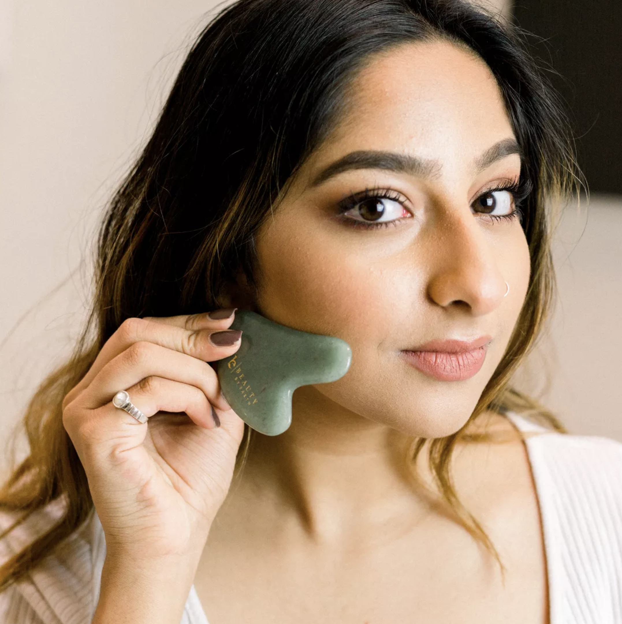 Model using a jade gua sha tool on their face