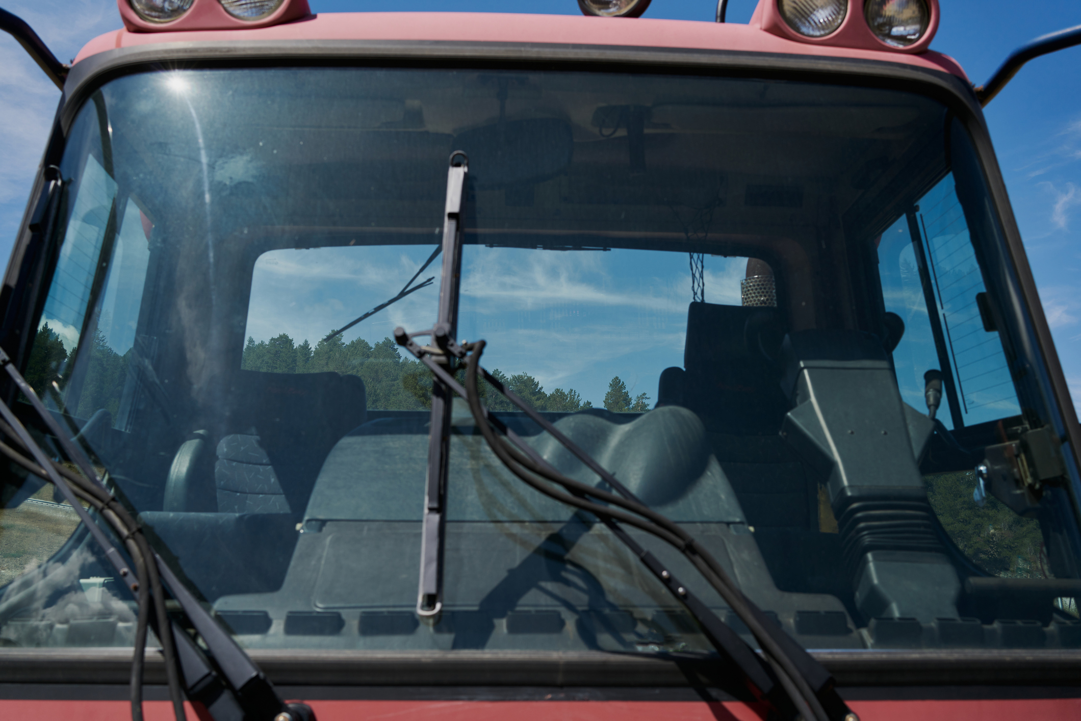 View through tractor windshield showing empty driver's seat and forest reflection