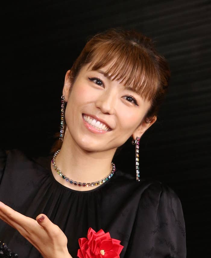 笑顔の女性がブラックドレスと赤い花のブローチを身に着けています。