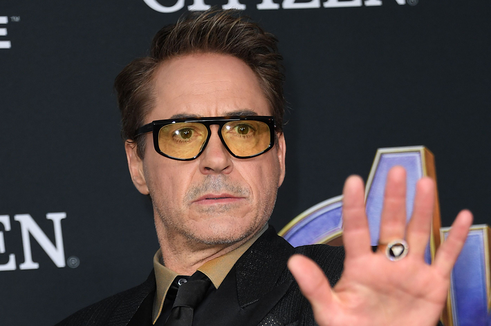Robert Downey Jr. raising his hand, wearing glasses and a suit at an event