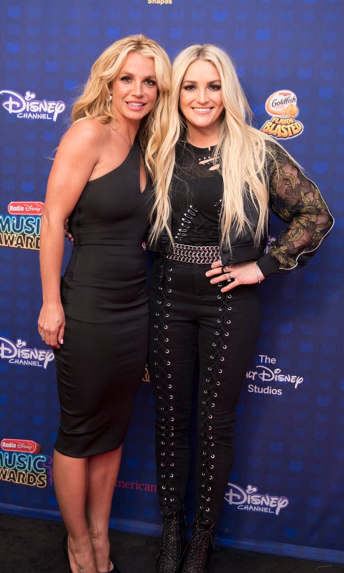 Britney Spears and Jamie Lynn Spears pose together; Britney in a black dress and Jamie Lynn in a black top and pants with embellishments