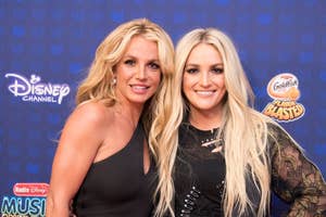 Two women smiling on a blue backdrop with Disney and music logos, one in a black sleeveless top, the other in a black lace outfit