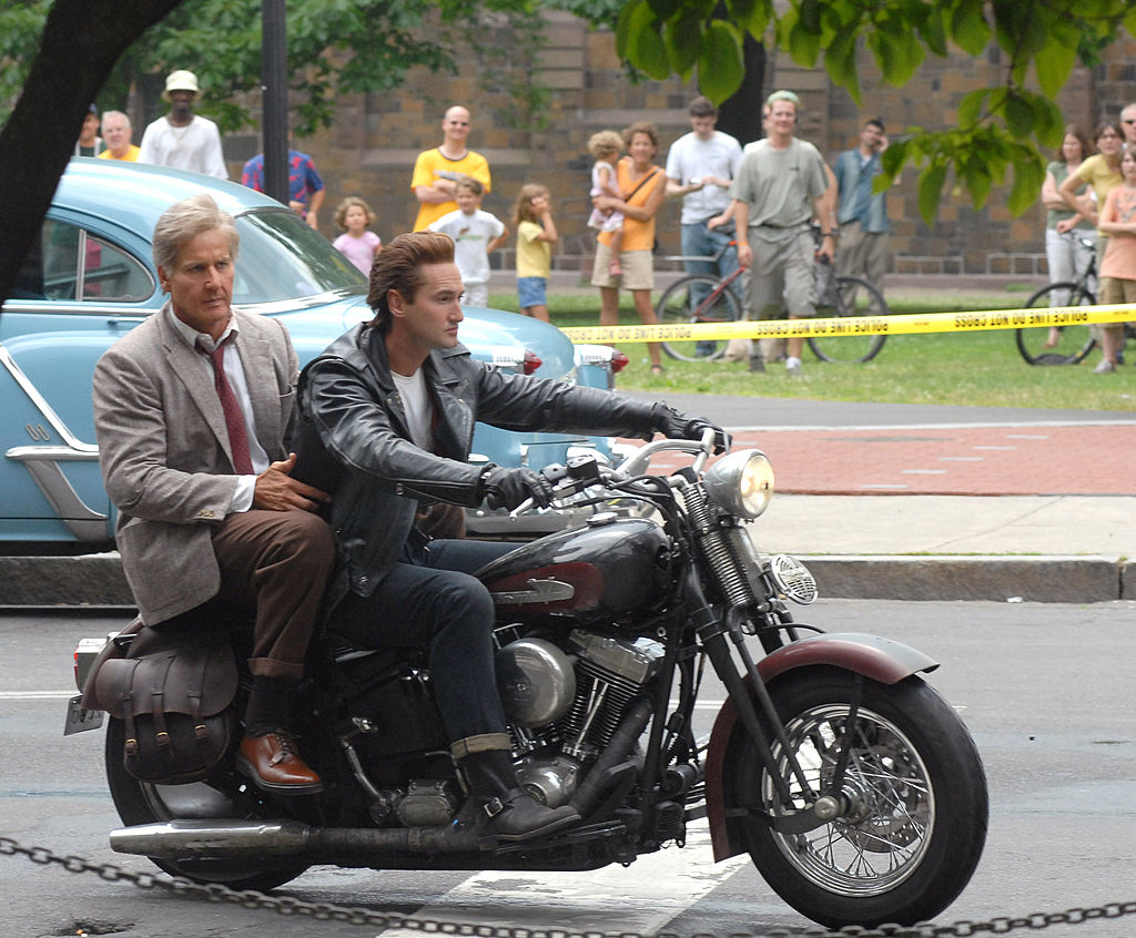 Harrison Ford and a stunt person riding a motorcycle on set, with spectators in the background