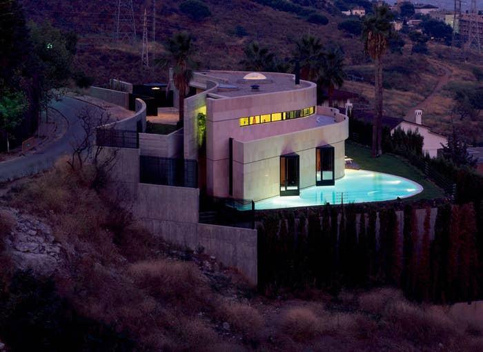 Modern house with geometric design and pool, lit at twilight, nestled in hills