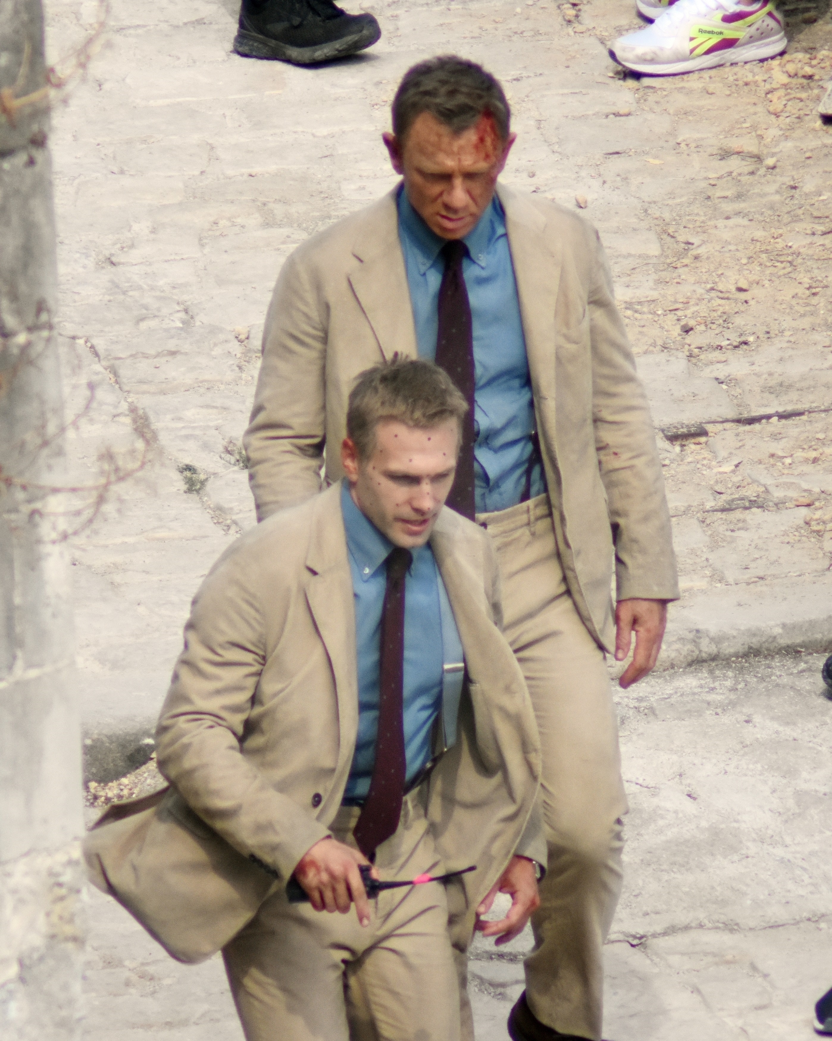 Daniel Craig and Jean-Charles Rousseau in distressed beige suits and blue ties on a film set