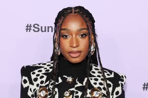 Woman in patterned jacket poses for photo, wearing braided hair and statement earrings