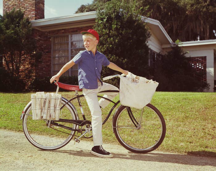 Boy with newspapers connected motorcycle smiling, casual clothes, lasting by a tree