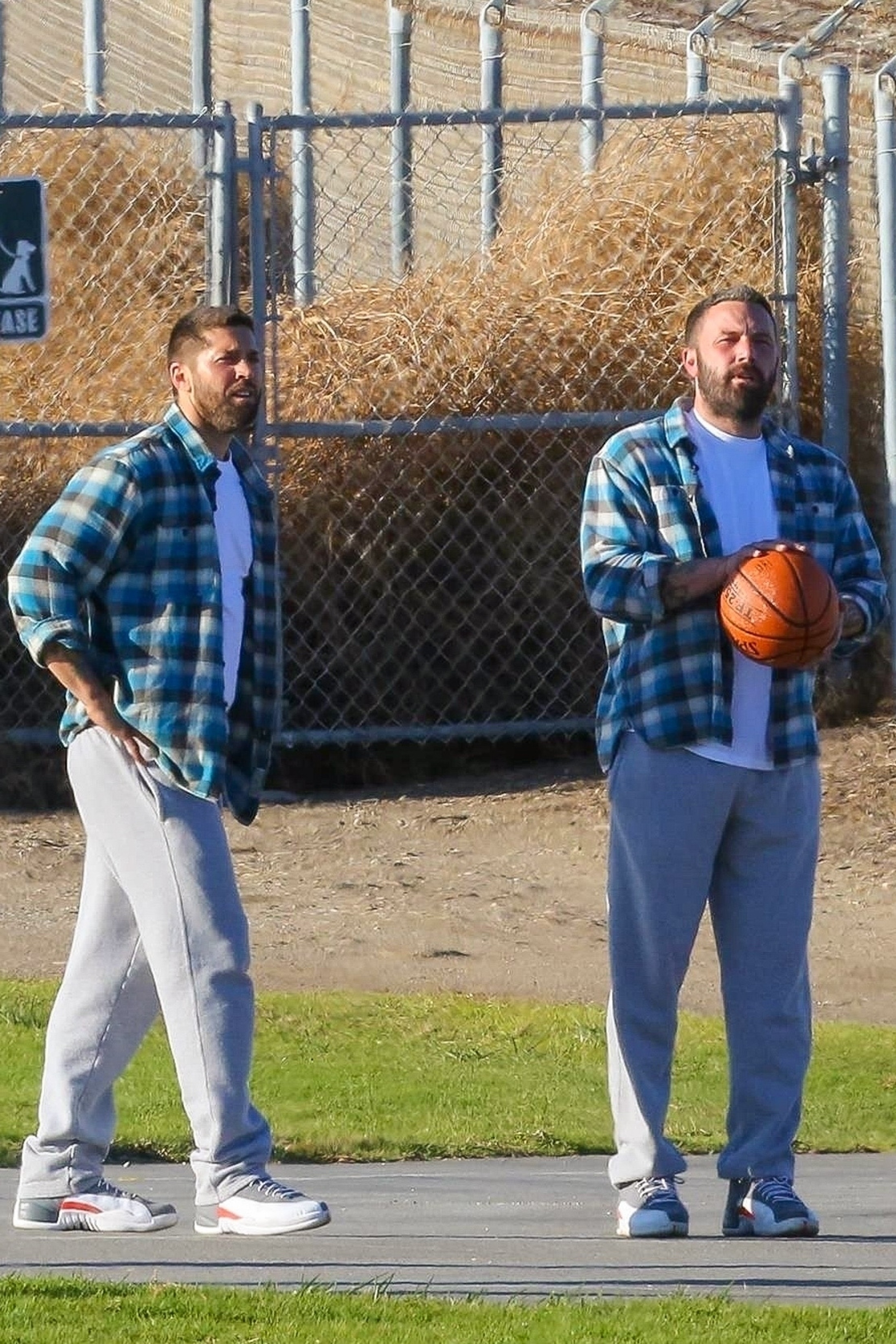 Two men standing on a basketball court, one holding a ball, dressed in casual attire