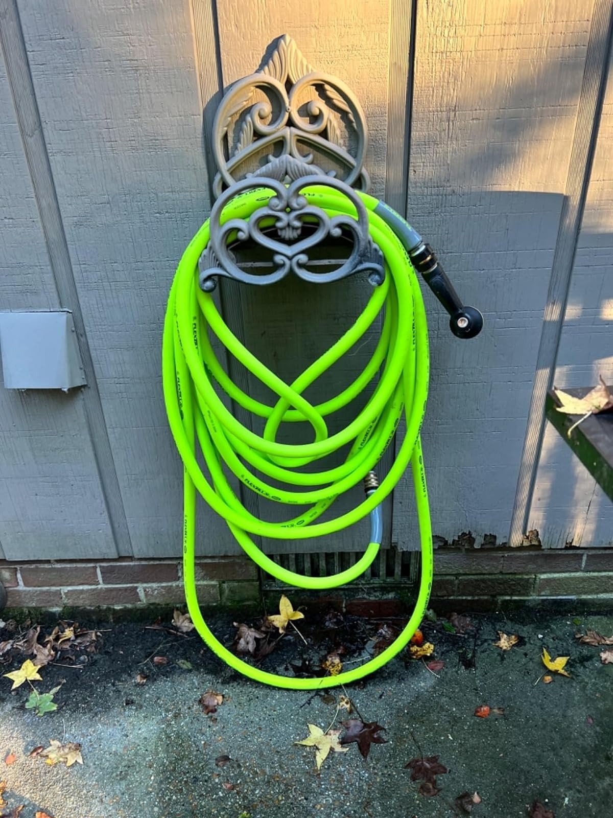 Bright neon garden hose coiled on a decorative holder attached to a wooden wall