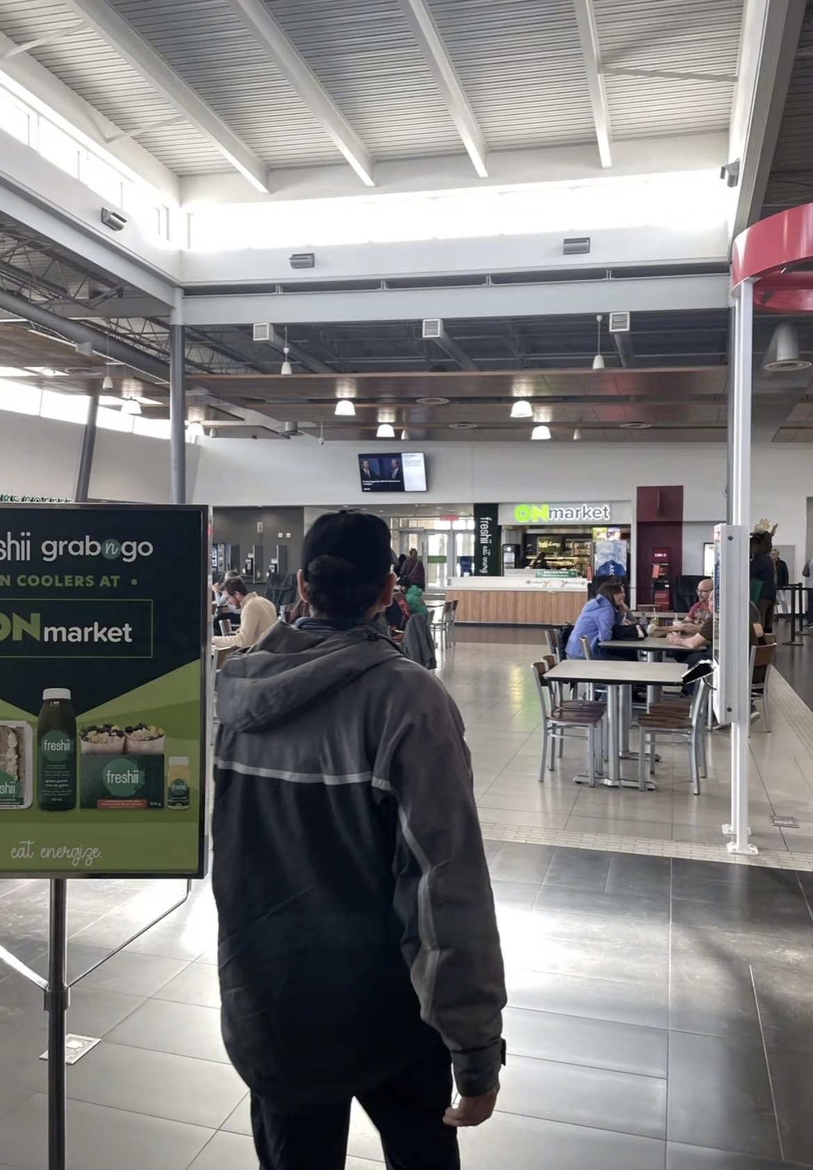 Person from behind looking towards a food court with various eateries and seated patrons